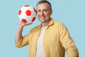 Handsome mature man with soccer ball on blue background