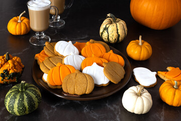 A plate of pumpkin-shaped cookies and a cup of latte on a dark background