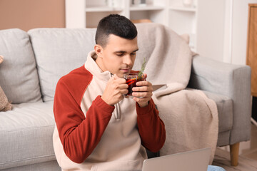 Handsome young man with glass of warm mulled wine in living room