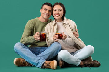 Happy couple with glasses of warm mulled wine sitting on turquoise background