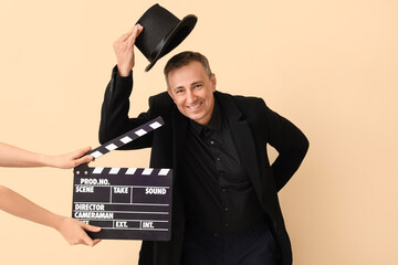 Mature actor and hands with clapperboard on beige background