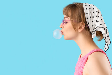Beautiful young woman with chewing gum on blue background, closeup