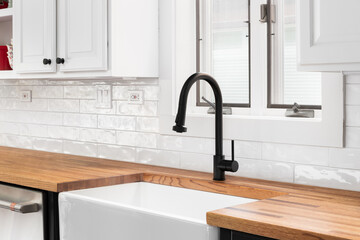 A kitchen faucet detail with white cabinets, a butcher block countertop, and a white subway tile...
