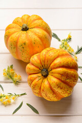 Fresh pumpkins and beautiful flowers on white wooden background