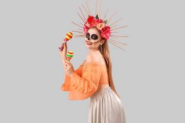 Young woman with maracas painted skull on her face against grey background. Celebration of Mexico's Day of the Dead (El Dia de Muertos)