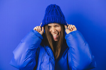 Beautiful brunette woman winter portrait isolated blue background. Model in casual blue puffer and...