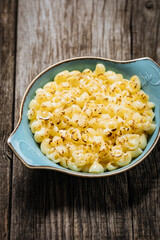 Mac and Cheese in blue bowl placed on rustic wooden board, with basil on top. 