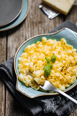 Mac and Cheese in blue bowl placed on rustic wooden board, with basil on top. 