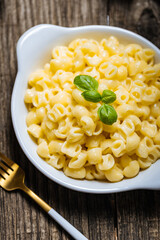 Mac and Cheese in blue bowl placed on rustic wooden board, with basil on top. 