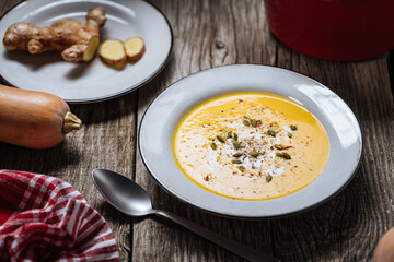 Creamy pumpkin soup garnished with  cooking sauce served in white bowl on rustic wooden background. Seasonal warm food. Autumn Appetiser 