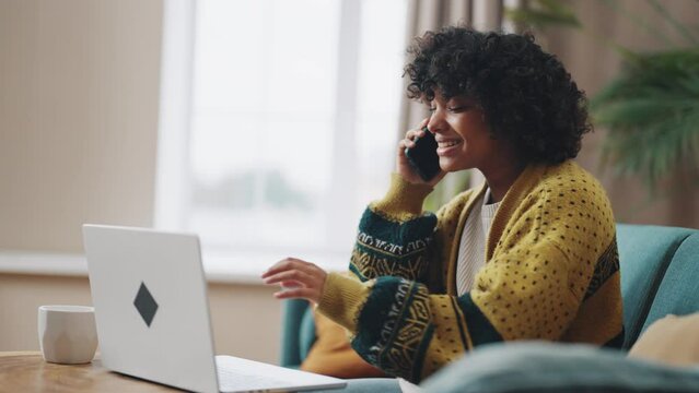 African American woman sitting in home office Smiling young girl using laptop and talking on mobile phone Happy businesswoman sitting behind laptop and mobile phone while working from home Work home