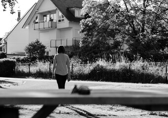 A young woman walks away from a house, deep in thought. The black and white filter adds a sense of...