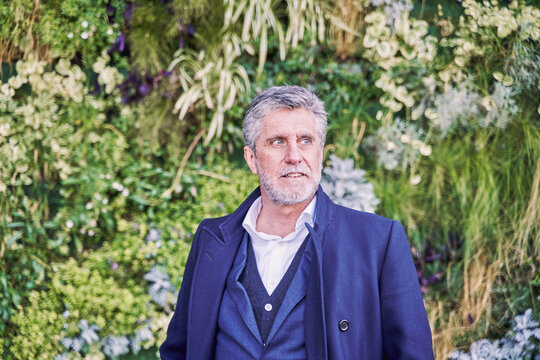 middle-aged gray-haired businessman posing on a background of green plants