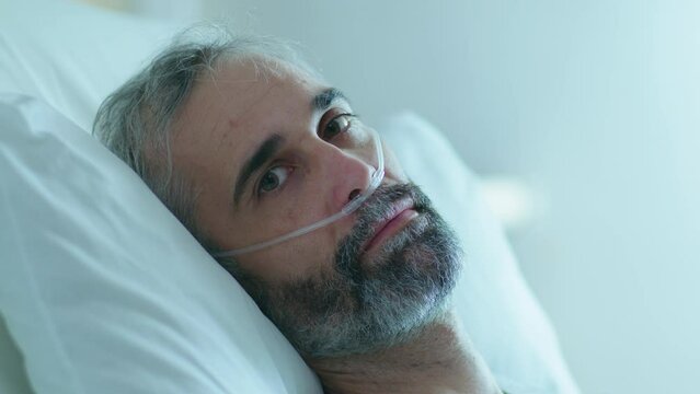 Middle Aged Man With Nasal Cannula Lying On Bed In A Hospital Ward And Looking At Camera. Zoom Shot, Video Portrait