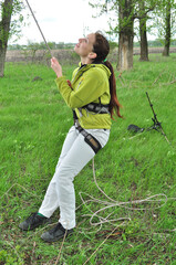 An athletic girl climbs a tall tree using a carabiner belay, pulls herself up onto the rope with her hands, and gains great height. Recreation and sports.