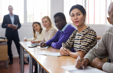 Concentrated asian woman listening to lecture in classroom with group of adult people. Postgraduate education concept..