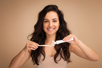 Cheerful brunette young woman holding teeth brush and toothpaste