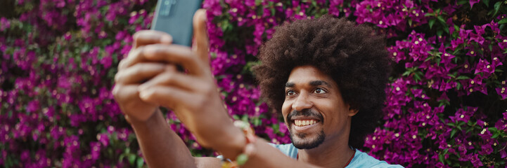 Close-up portrait of young African American man shooting selfie use smartphone stands on background...
