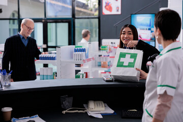 Drugstore cashier giving client shopping bag with medicine at checkout. Smiling casian woman taking purchase package from pharmaceutical employee at medical retail store counter desk