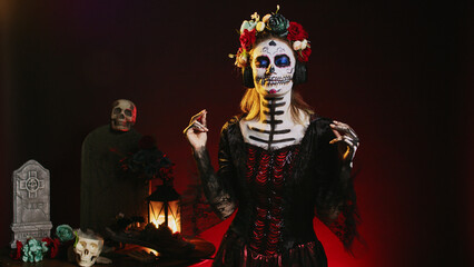 Goddess of dead enjoying music on headphones, wearing skull make up and santa muerte costume in studio. Beautiful person listening to song on audio headset, celebrating day of the dead.