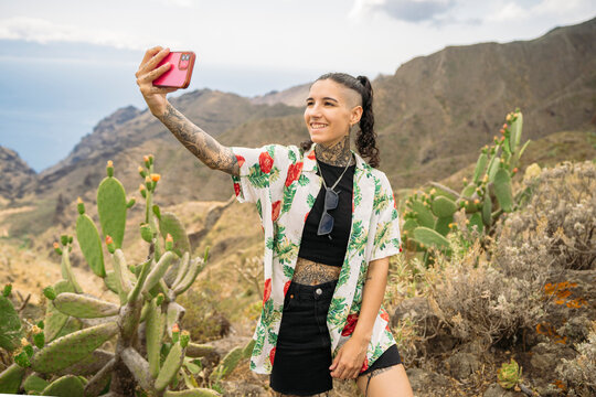 Tattooed woman taking selfie against mountains
