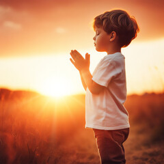 Fototapeta na wymiar child praying with hands together, at sunset in the field outdoors in a summer day