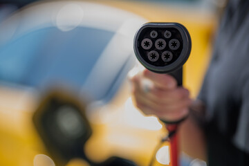 Anonymous person standing with charging power to electric vehicle at gas station