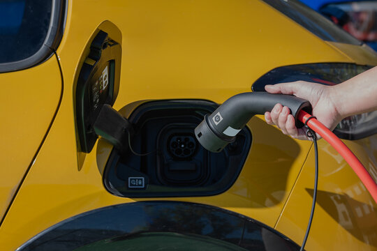Anonymous person standing inserting charging power cable to electric vehicle at gas station