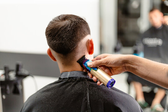 Barber cutting client's hair with a multicolored clipper in salon.