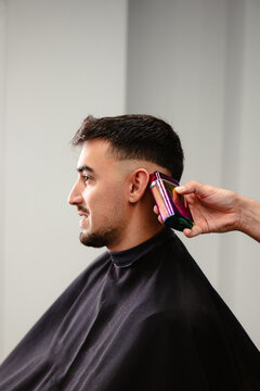Barber using electric clippers for male client's hair trim.