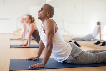 Hispanic man practicing yoga postures during group training at gym, performing stretching asana...