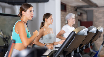 Young athletic woman training by running on treadmill in gym