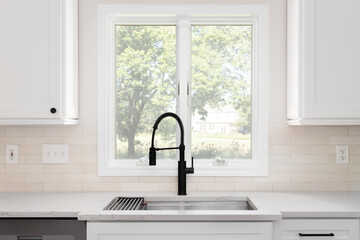 A black faucet detail with white cabinets, brown subway tile backsplash, and white marble...