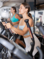 Fototapeta premium Slender athletic girl during cardio exercises on elliptical simulator in fitness center. Sports to max. Electronic tracking for most productive workout
