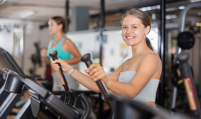 Fototapeta na wymiar Young sporty girl working out on elliptical machine in gym. Healthy active lifestyle concept