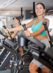 Fototapeta premium Slender athletic girl during cardio exercises on elliptical simulator in fitness center. Sports to max. Electronic tracking for most productive workout