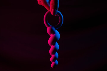 Woman holding anal beads in neon pink blue light. Copy space. 