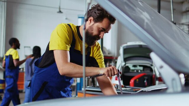 Licensed repairman in car service picks torque wrench from work station bench, using it to tighten bolts after replacing engine. Garage worker uses professional tools to fix client automobile