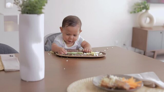 Baby led weaning concept. Baby eating with his hands sitting at the table, with a preloaded spoon