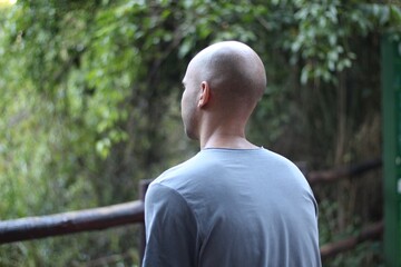 bald man with his back in a gray shirt observing the green nature, Brasília, 2023