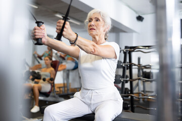 Elderly athletic woman in sportswear working out using straps in gym