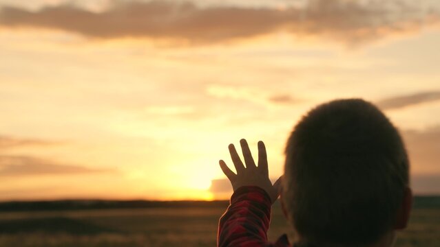 Kid Boy stretches his hand to beautiful sky, dream in nature. Child is playing. Hand of child boy stretches to beautiful sky, sunset. Children dream hopes, reach out your hands to sky. Children prayer
