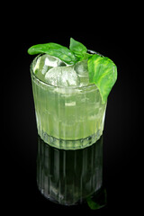 BASILIC SMASH is an interesting modern cocktail with intense basil flavor, which is prepared on the basis of gin. Drink in a glass on dark background with reflection