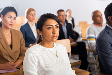 Young adult female attentively listening to motivation lecture with colleagues at conference