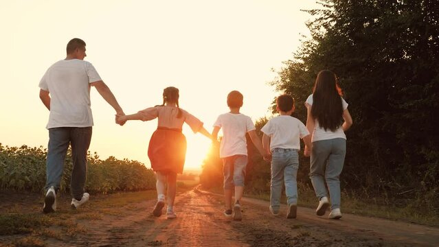 Sportive family with little children run joining hands along road at sunset
