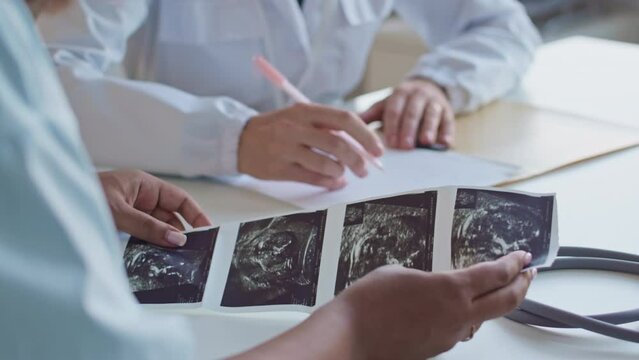 Cropped shot of unrecognizable pregnant woman and gynecologist sitting at desk in hospital office and discussing baby ultrasound image