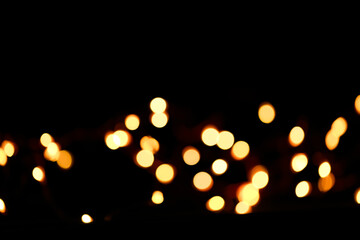 Yellow bokeh on a black background. New Year and Christmas Festive background.Warm bokeh festive background.