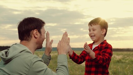 Cheerful boy high-fives father standing in middle of field at sunset twilight