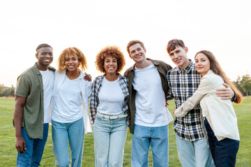 group of multiracial young people standing together and hugging in the park and looking at the camera, team of students