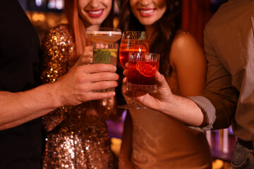 Friends clinking glasses with fresh cocktails in bar, closeup